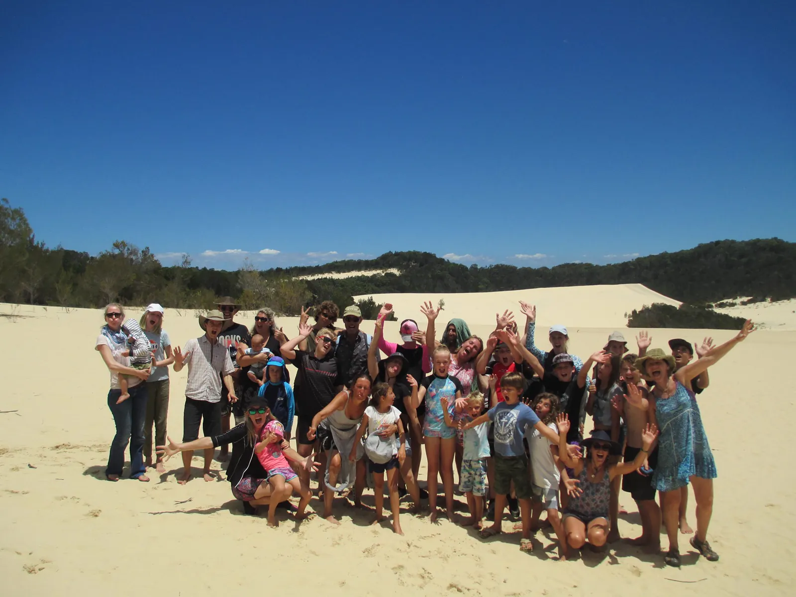 A large group of families on a sand dune, arms in the air